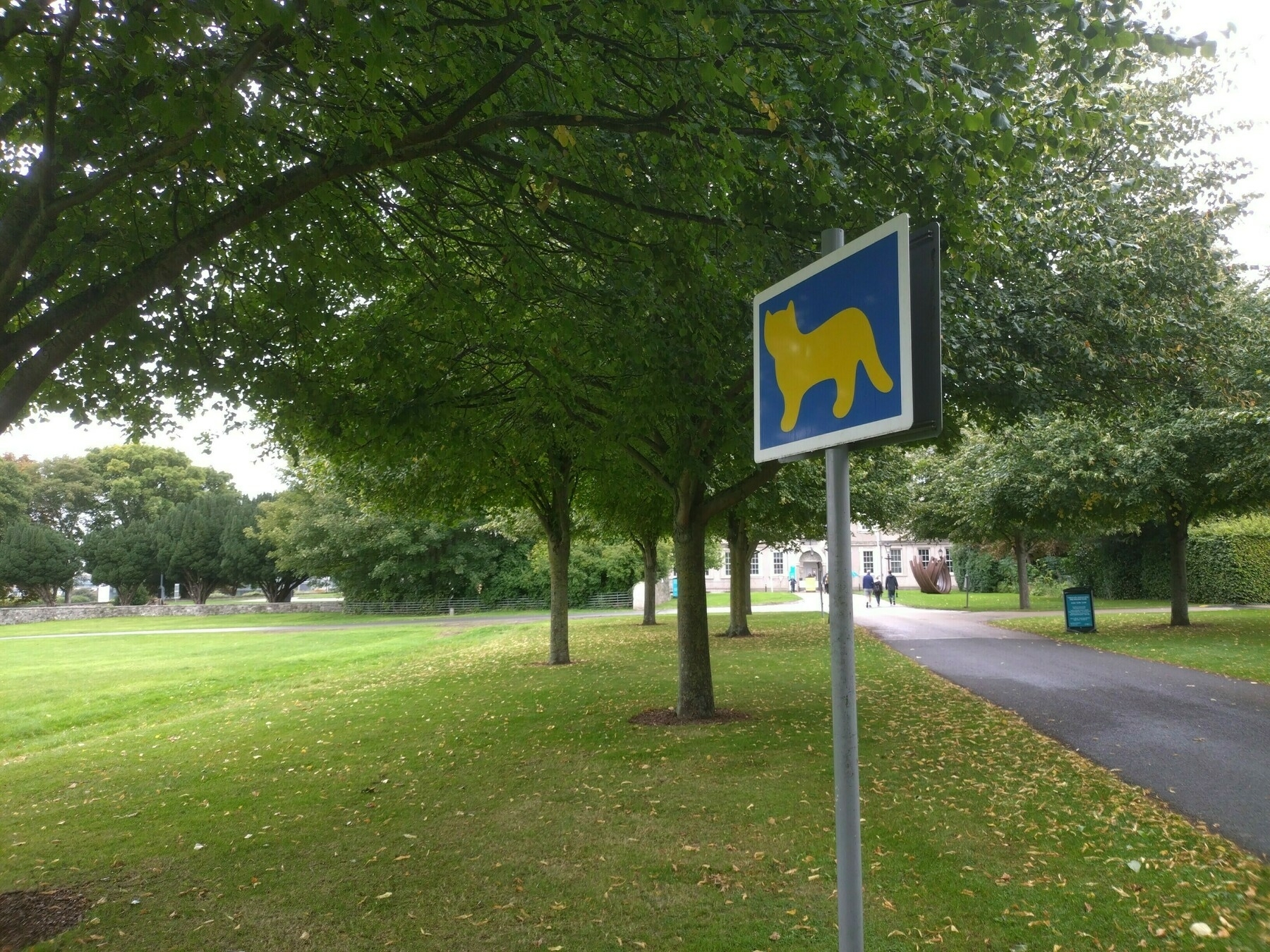 A park pathway with a humorous sign featuring a yellow cat silhouette on a blue background.